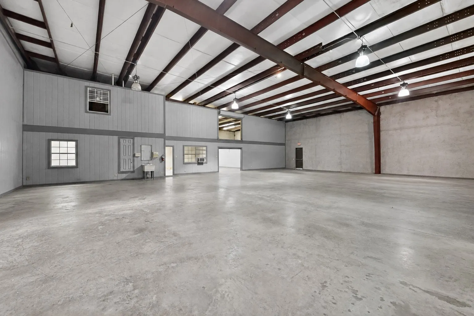 Expansive open-concept space featuring concrete flooring, exposed metal beam ceiling structure, and multiple windows with grid detailing