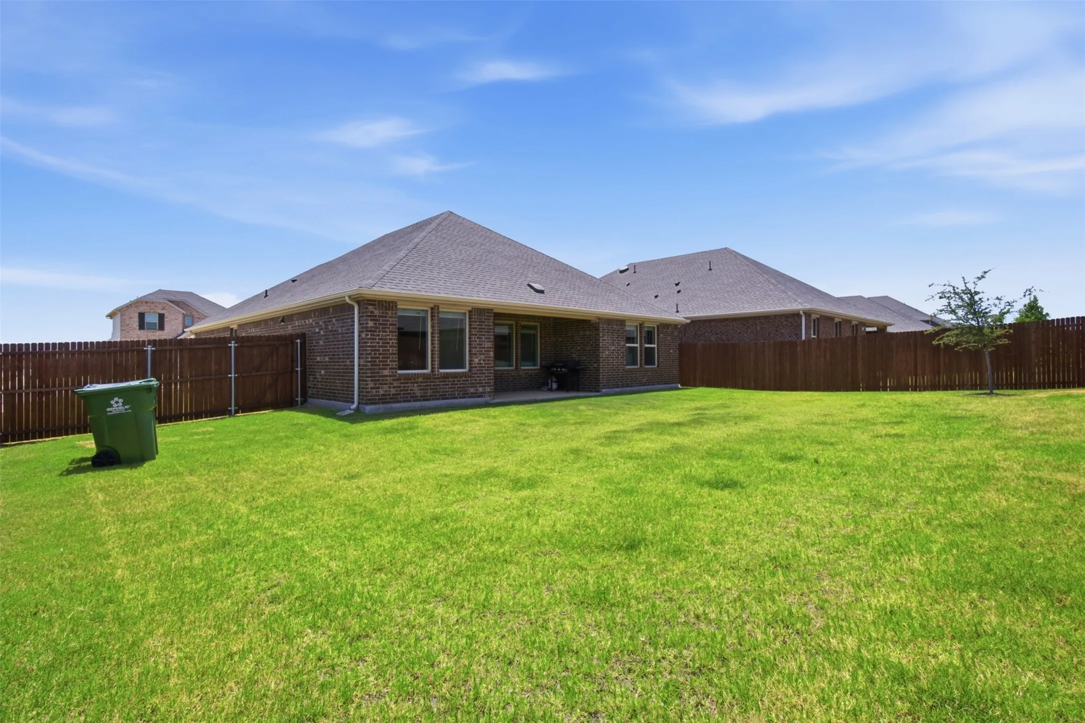 Expansive backyard featuring a lush green lawn, full privacy fencing, and a covered patio area