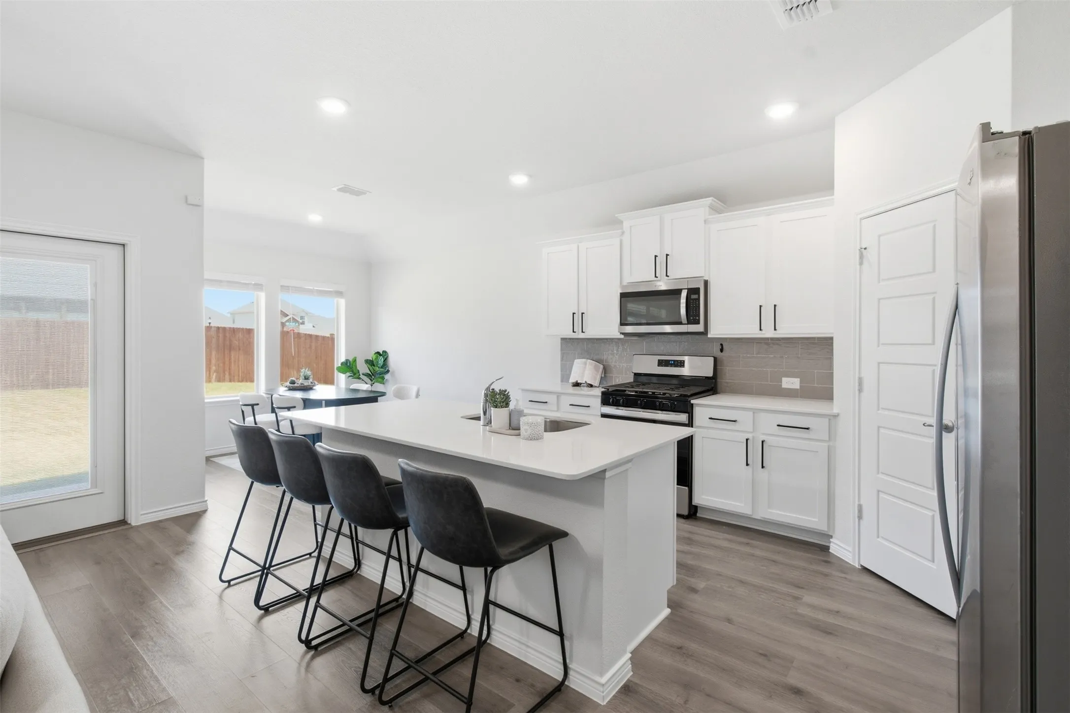 Contemporary kitchen featuring a large island with seating, white cabinetry, integrated stainless steel appliances, and wood-finish flooring