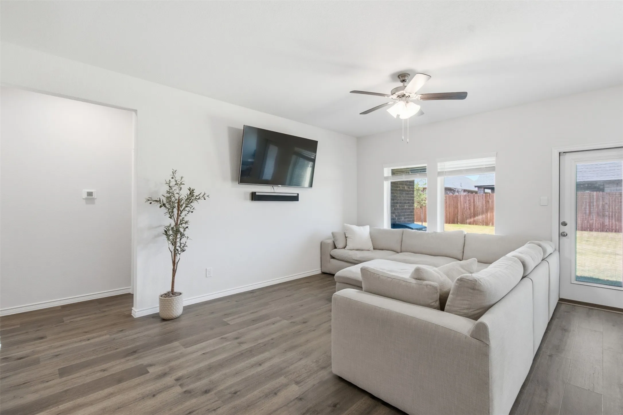 Spacious living area featuring wood-finish flooring, white walls, and a ceiling fan with integrated lighting