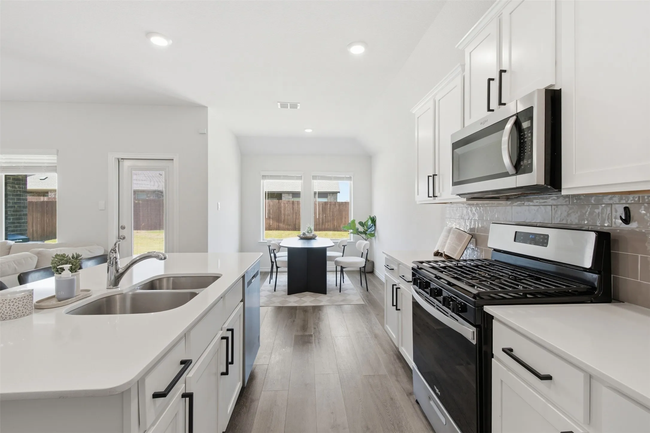 Modern kitchen featuring white shaker cabinetry with matte black hardware, stainless steel appliances, a double basin sink, and wood-finish flooring