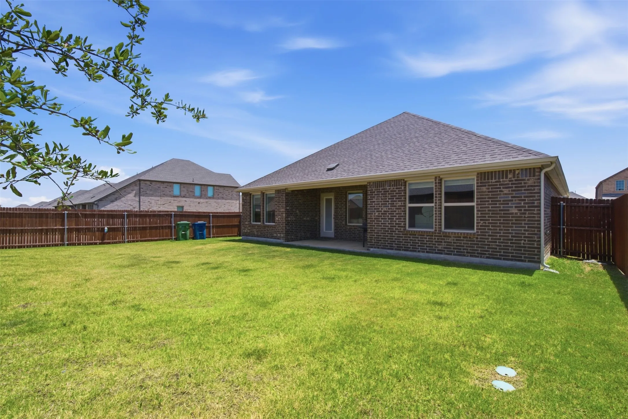Spacious backyard featuring a large green lawn, a covered patio, and privacy fencing