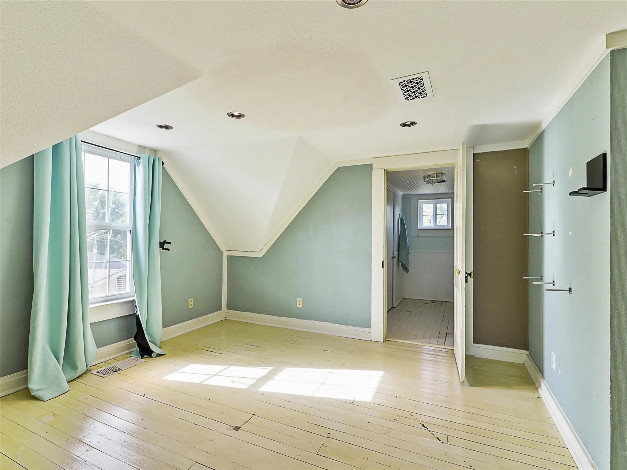 Attic room with painted light wood plank flooring and two windows