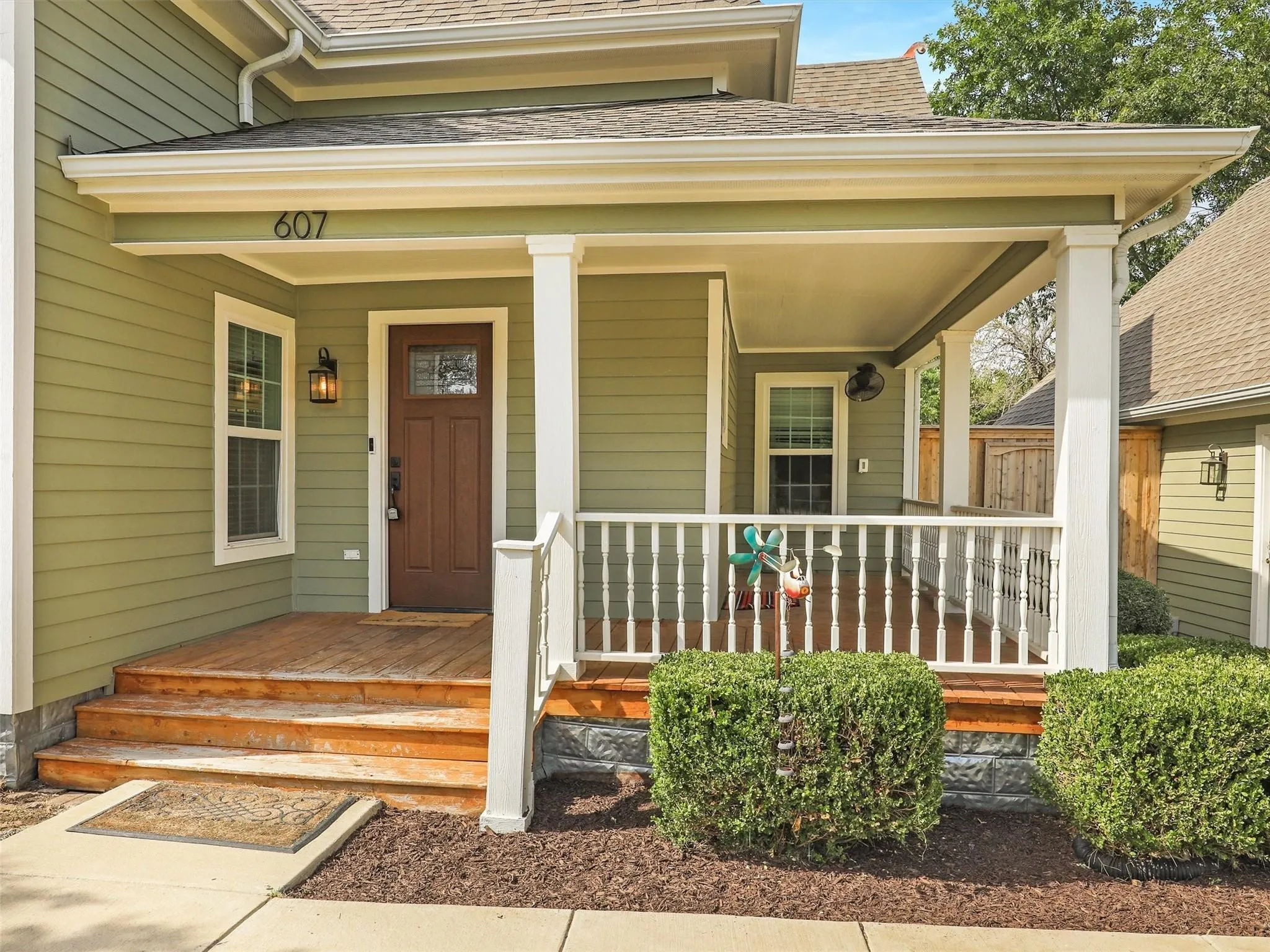 Covered front porch with wood-finish decking and steps, white railing, and a wood-panel entry door with decorative glass