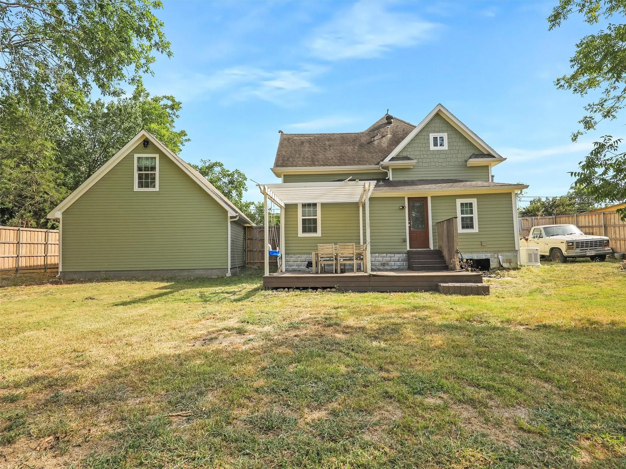 Rear exterior featuring a spacious wooden deck with an attached pergola, a separate gabled outbuilding, and wood-paneled fencing