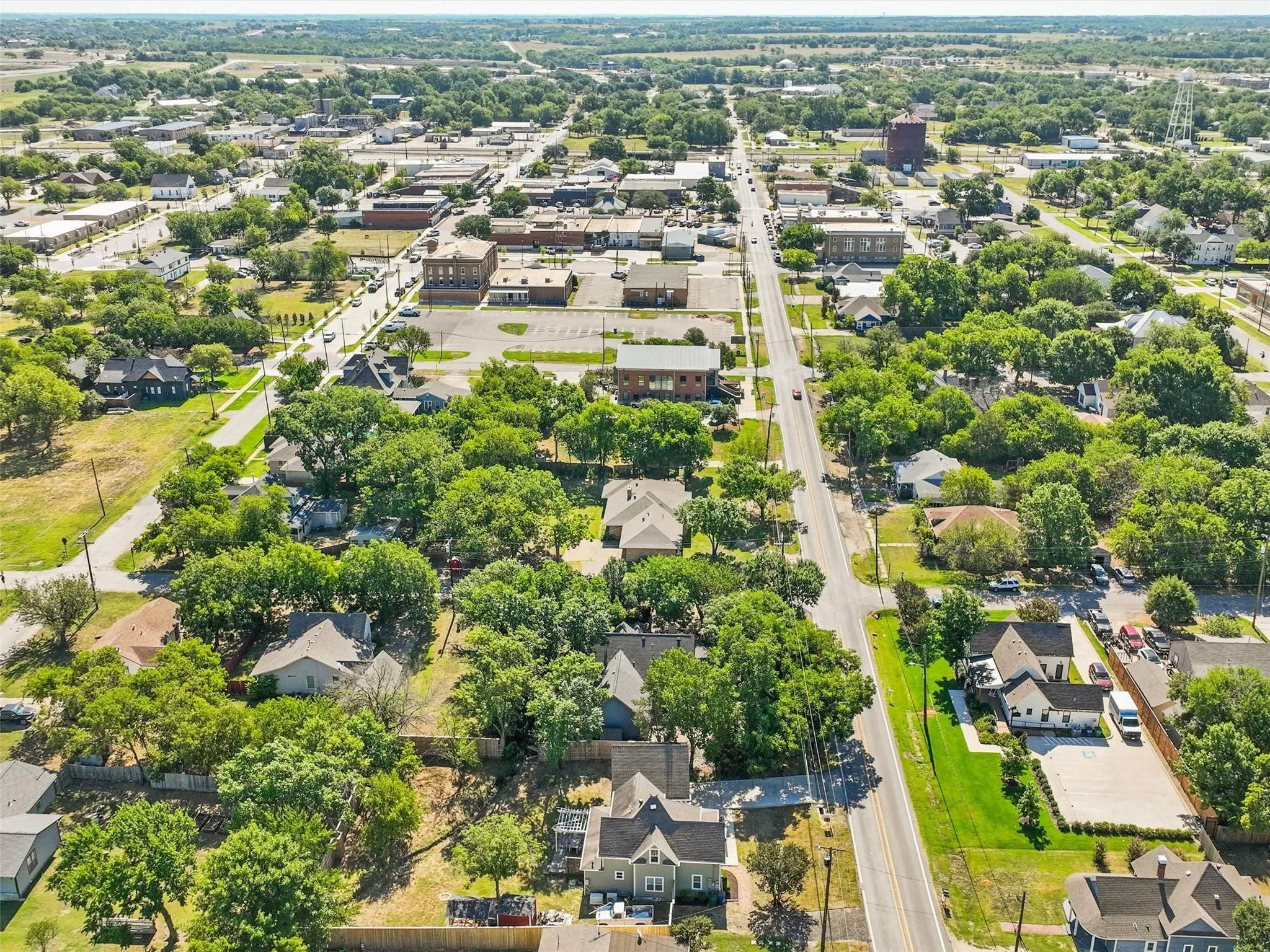 Aerial perspective showcasing a residential area featuring numerous mature trees, a central thoroughfare, and a mix of single-story and multi-story homes