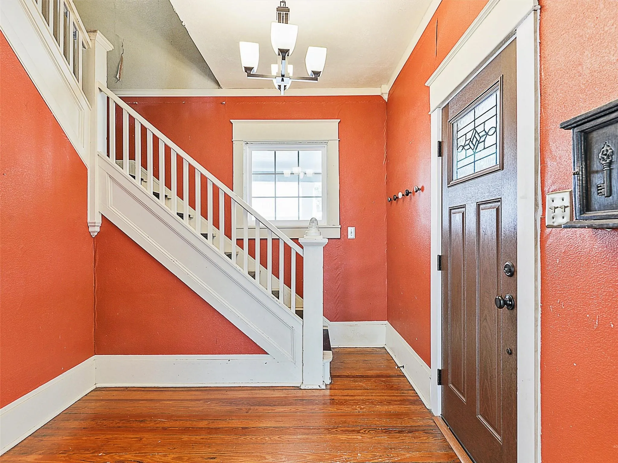 Entryway featuring wood-finish flooring, a white-balustrade staircase, and a dark wood door with a decorative leaded glass insert