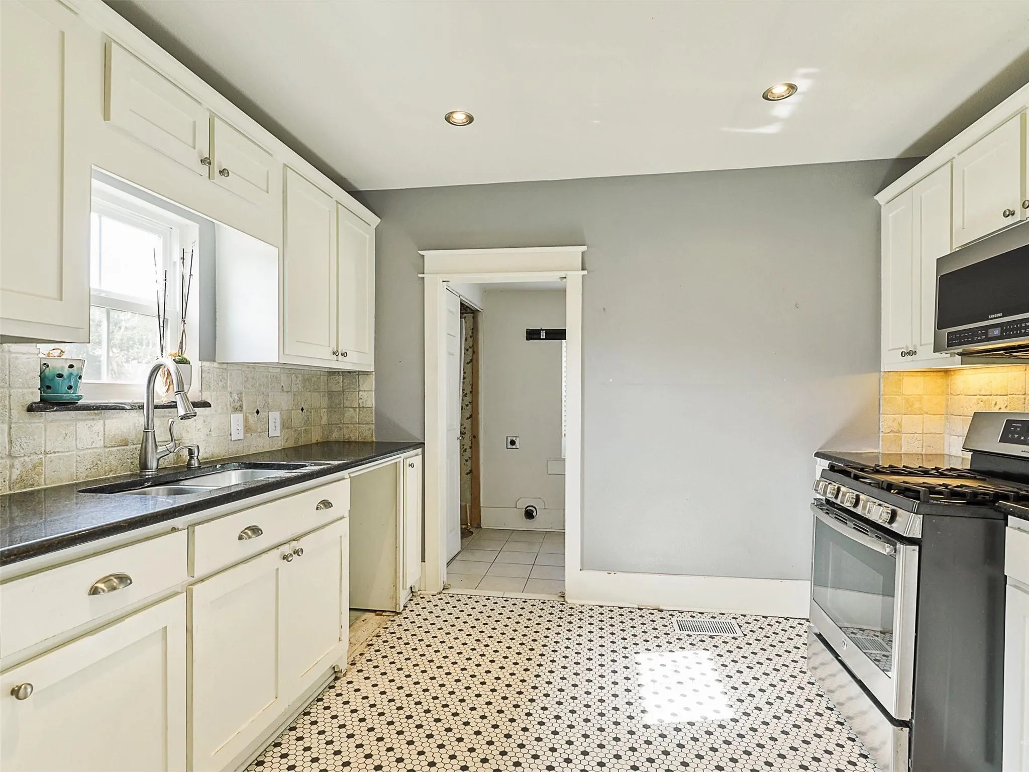 Kitchen featuring white shaker-style cabinetry, dark countertops, a mosaic tile backsplash, and a stainless steel appliance suite