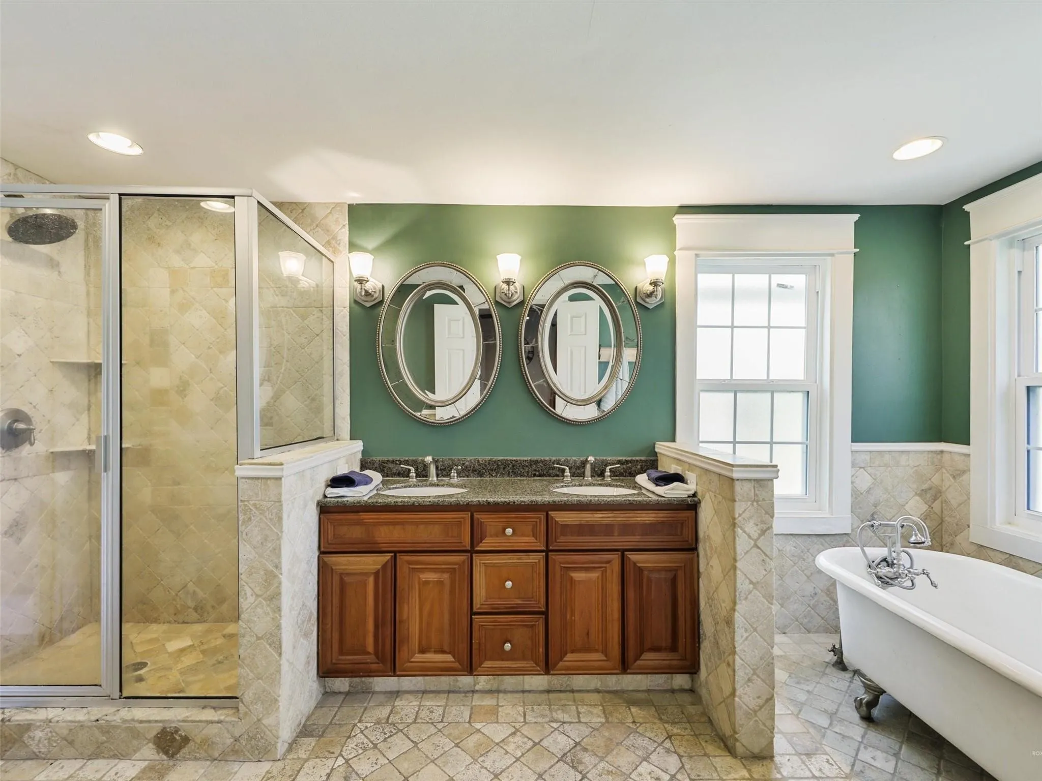 Bathroom featuring a glass-enclosed shower with tile surround, a dual vanity with wood cabinetry and stone countertop, and a freestanding clawfoot bathtub