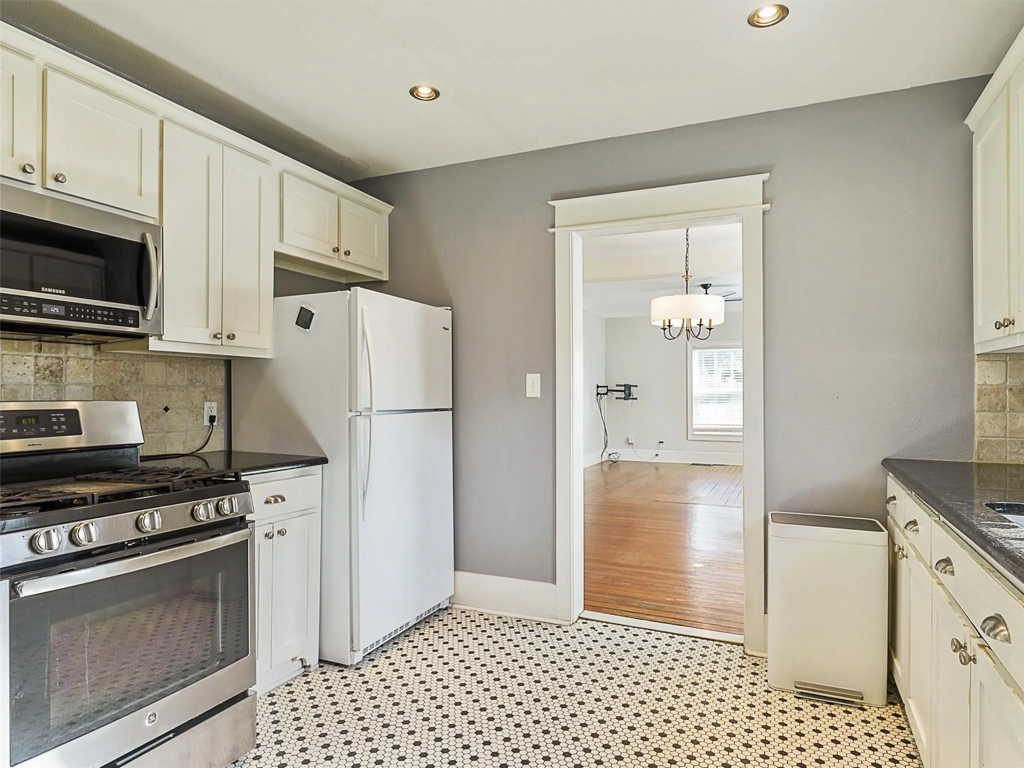 Kitchen featuring white cabinetry, dark countertops, a stainless steel range with overhead microwave, a white refrigerator, and black and white patterned tile flooring