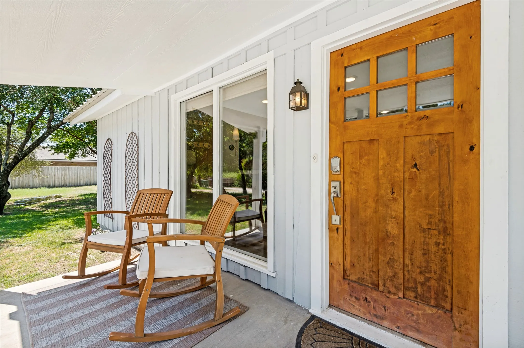 Front porch featuring rocking chairs, decorative wood front door, and exterior security camera with integrated floodlights.