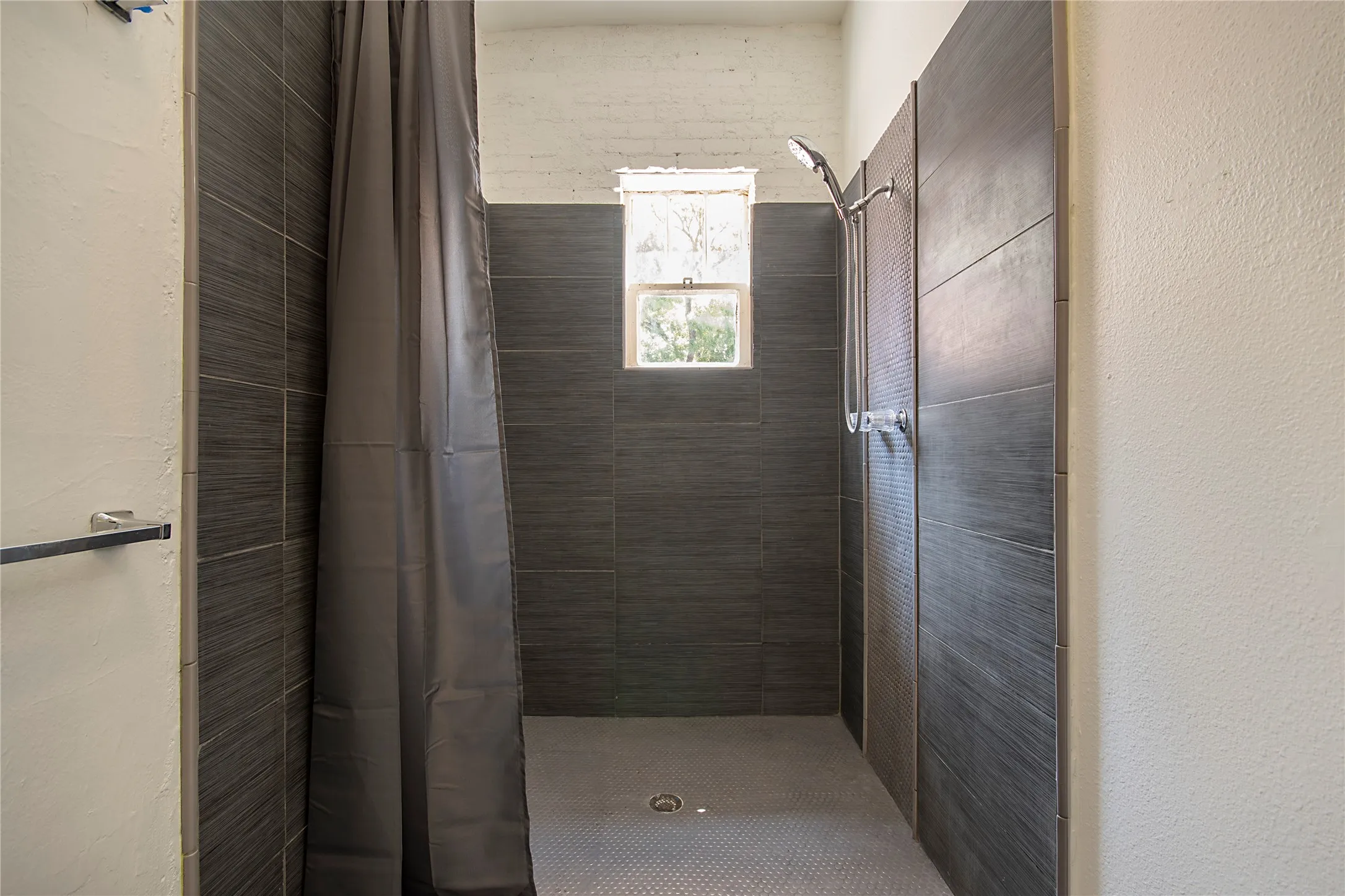 Shower stall featuring dark gray horizontal tile, a window, and a rain shower head
