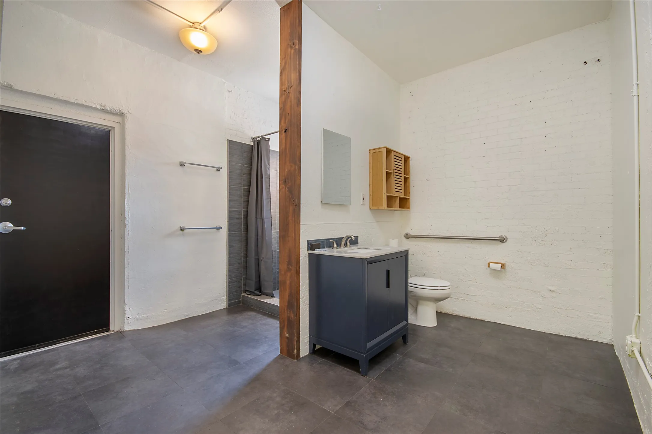 Spacious bathroom featuring dark gray tile flooring, a shower with gray subway tile surround, and a navy vanity with a white countertop
