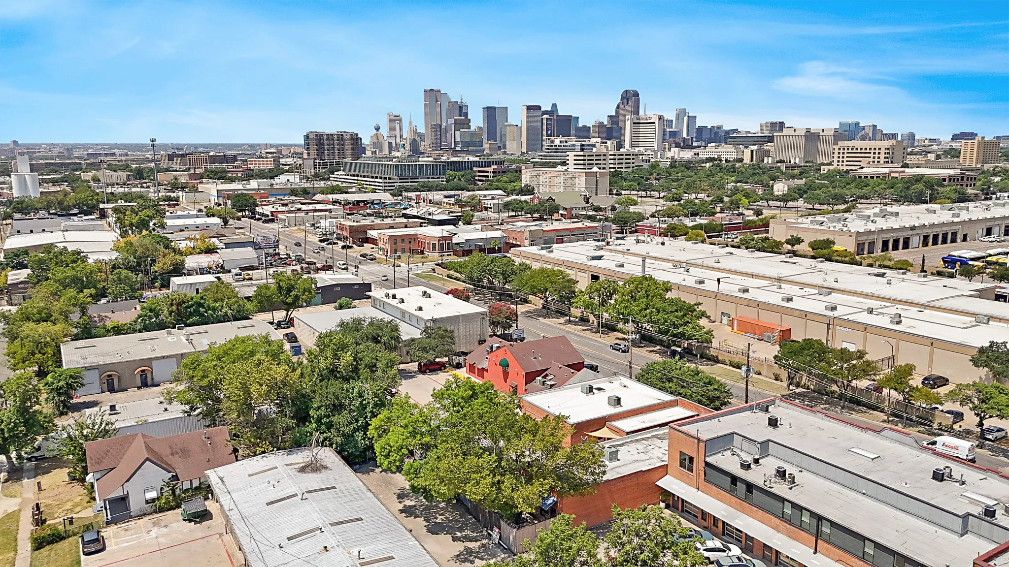 Urban landscape featuring a distant city skyline, commercial buildings, and mature trees under a clear sky