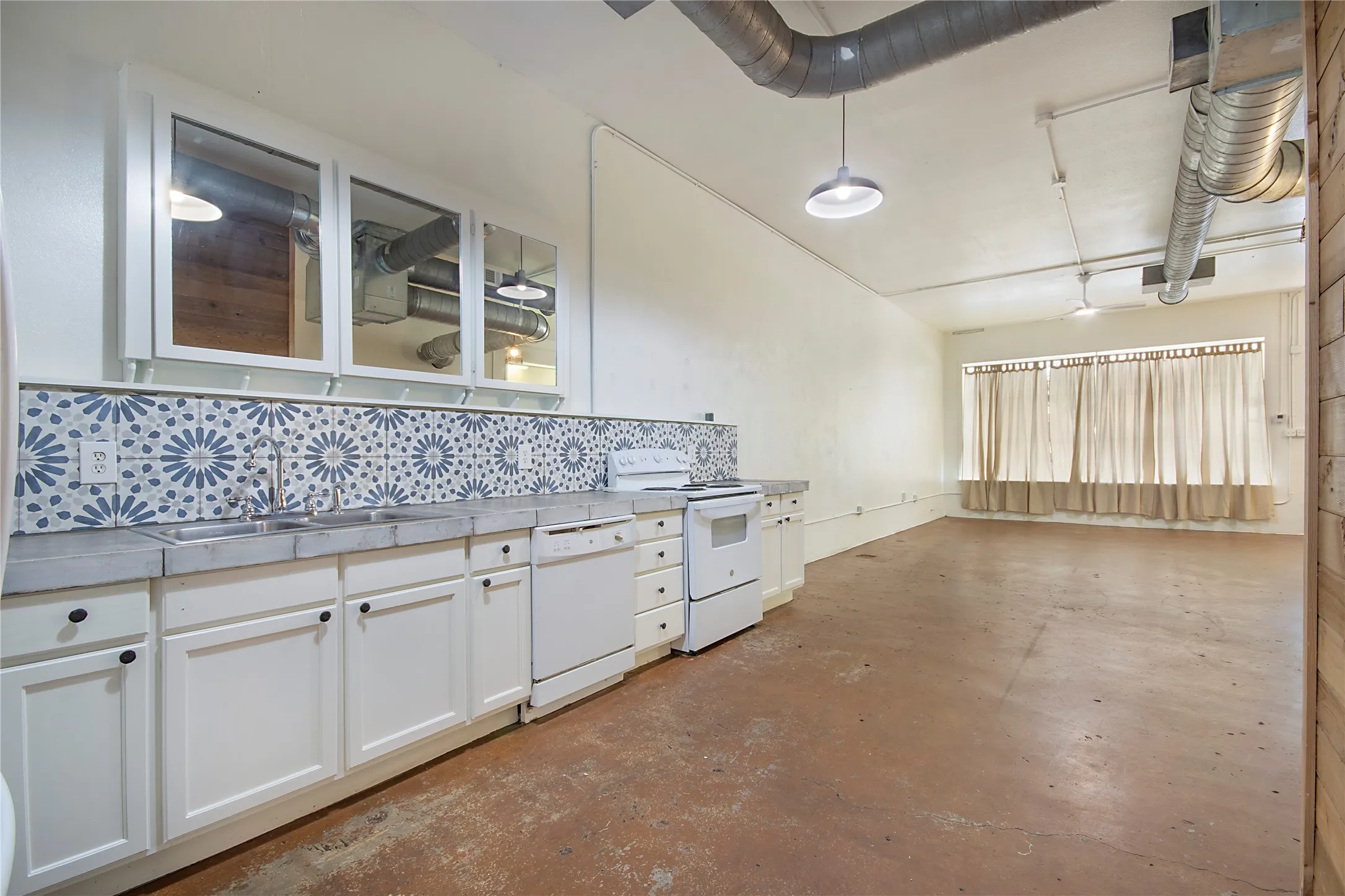 Functional kitchen area with patterned tile backsplash, white cabinetry, integrated double basin sink, and a white oven range