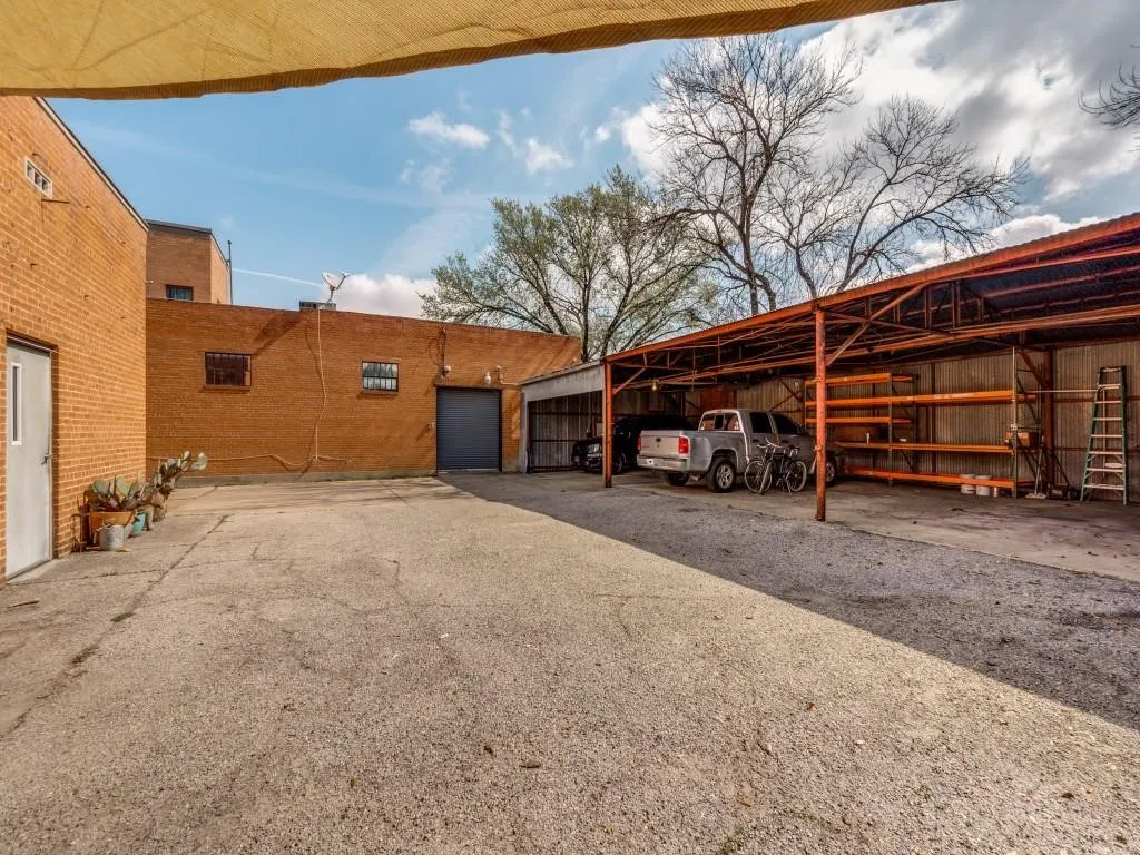 Spacious gravel and paved lot featuring a large covered storage area, a roll-up garage door, and brick building facades