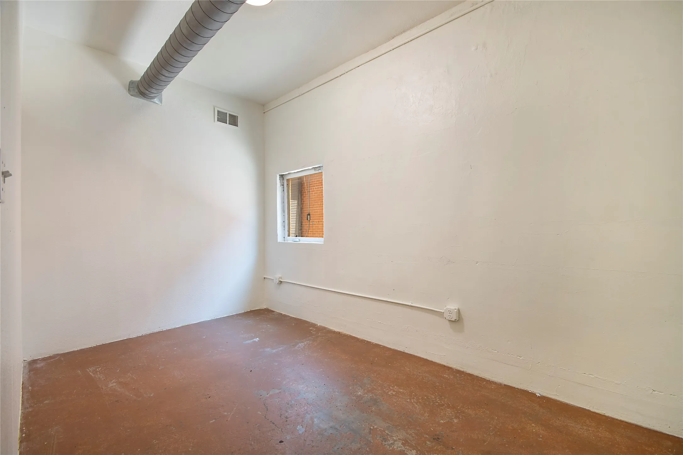 Room featuring a small window, exposed overhead ductwork, and concrete flooring