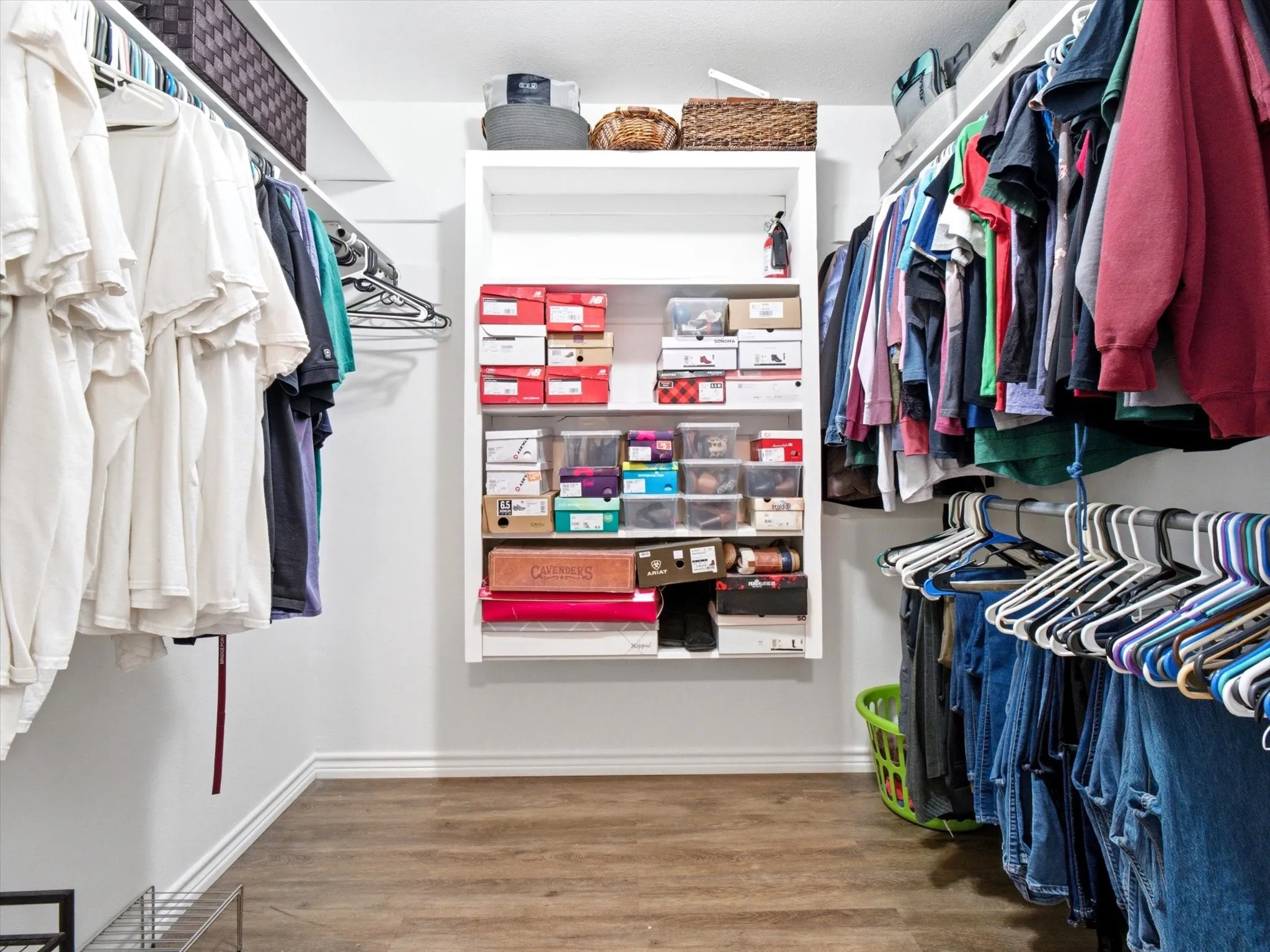 Walk-in closet featuring wood-finish flooring, white walls, and extensive built-in shelving and hanging rods