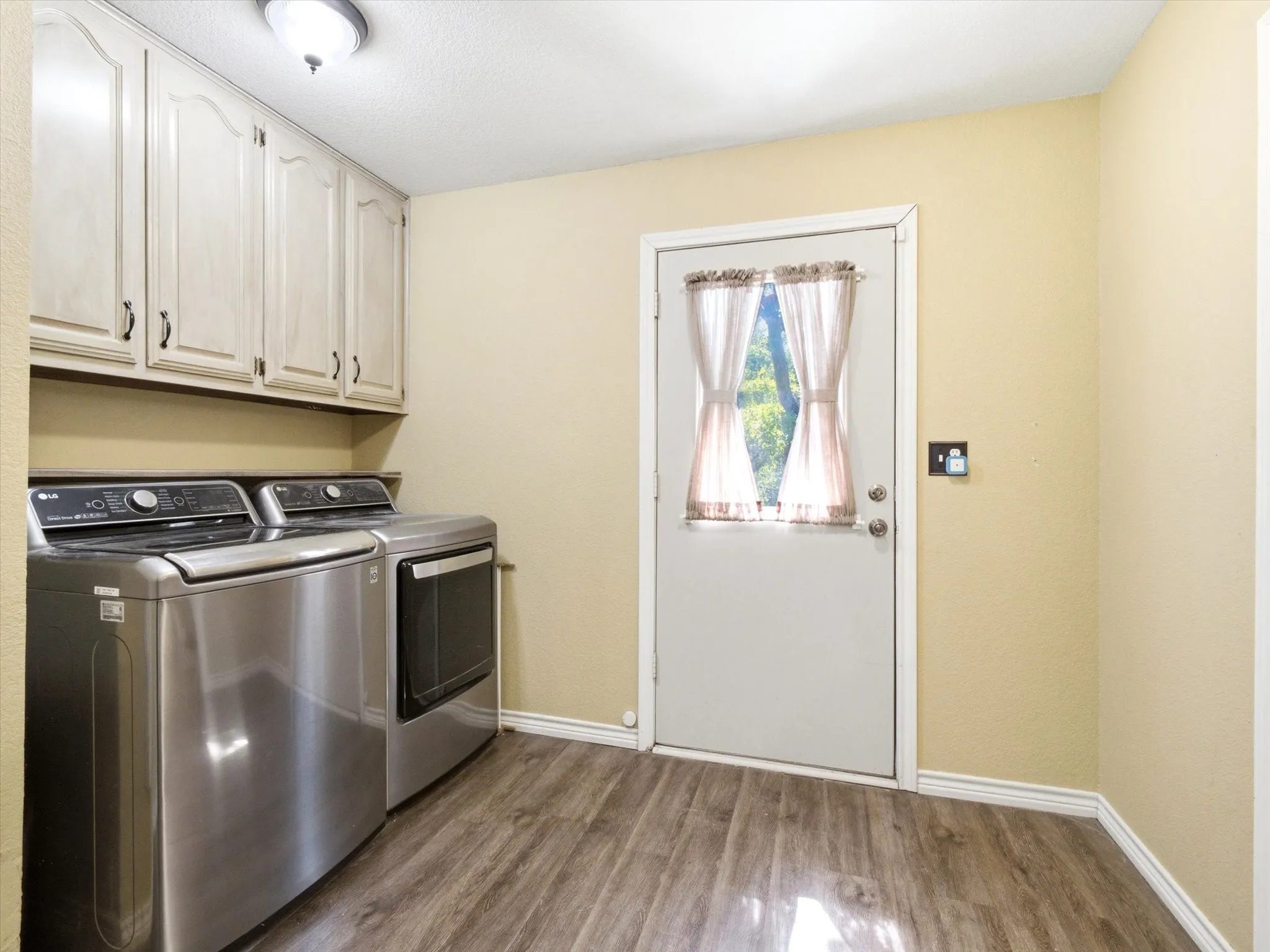 Dedicated utility space featuring overhead cabinetry, wood-finish flooring, a ceiling-mounted light fixture, and a white exterior door with a window insert