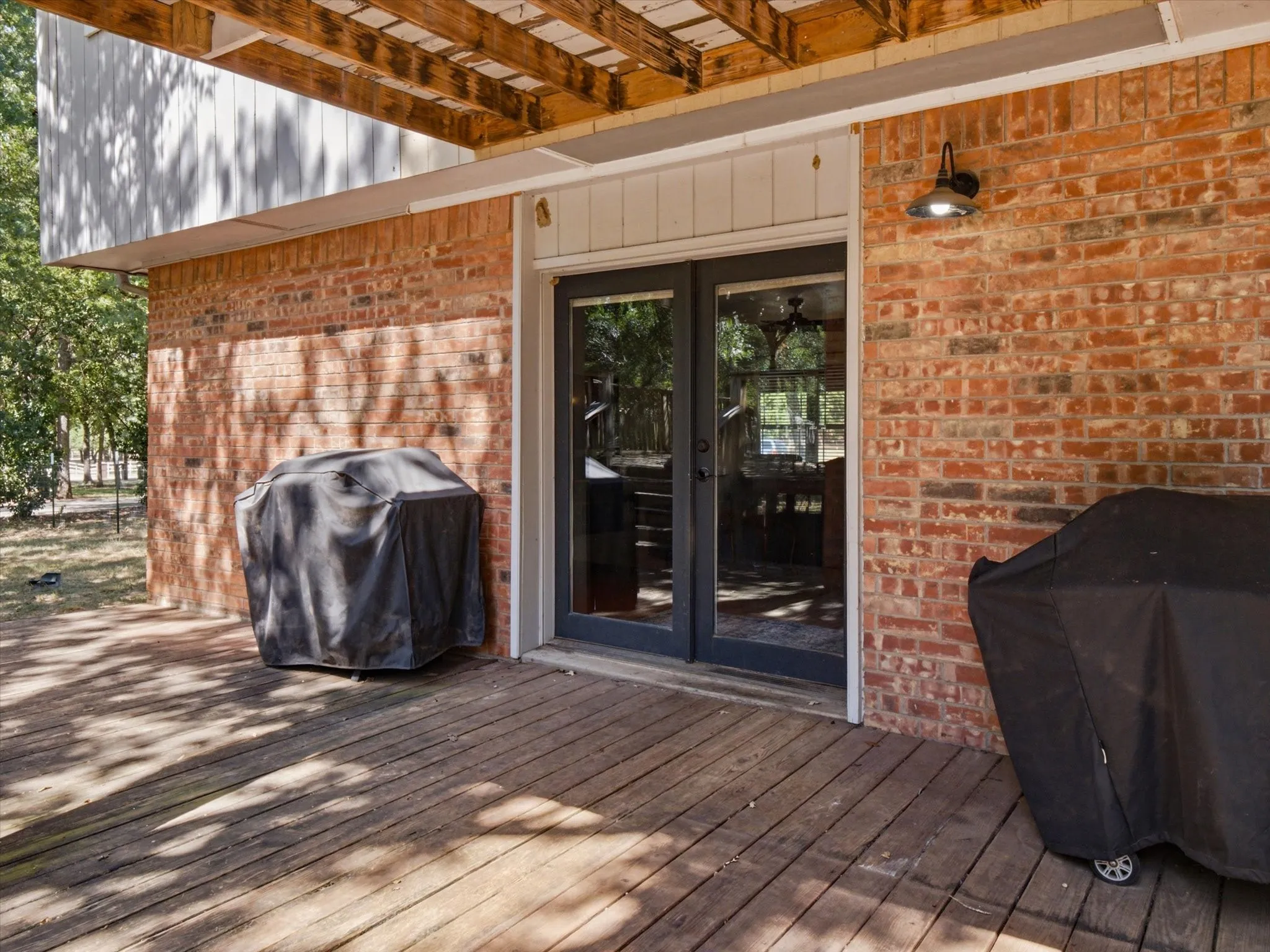 Wood-finish deck with red brick exterior and black-framed French doors