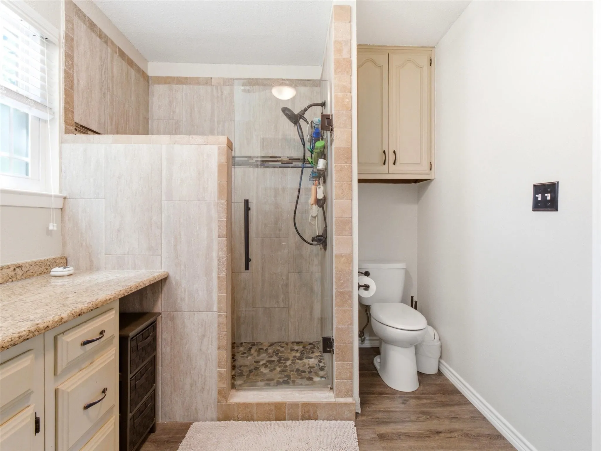 Walk-in shower featuring glass enclosure, stone-finish tile surround, and river rock flooring