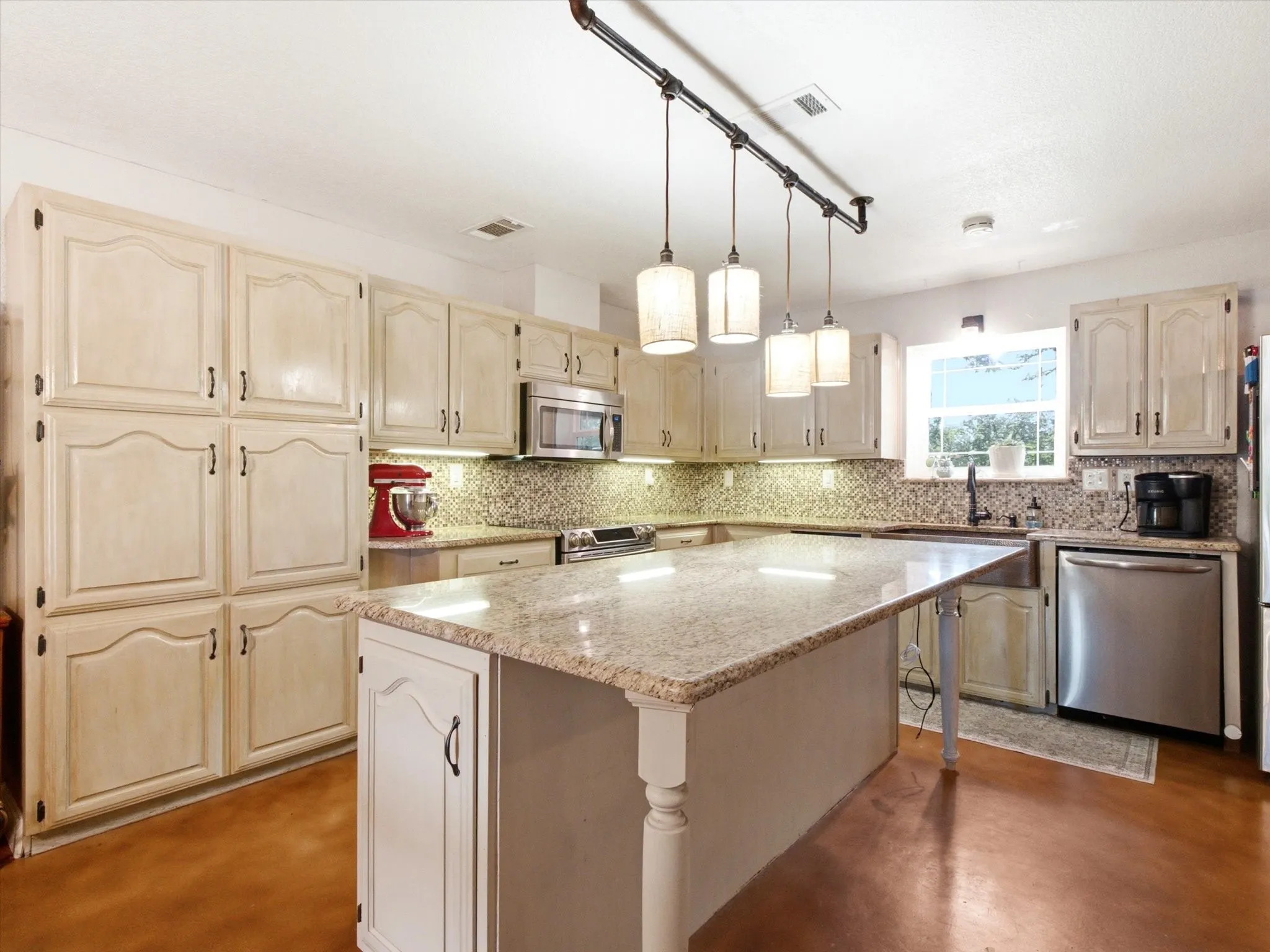 Kitchen featuring an oversized center island with a light-toned countertop, extensive cabinetry, a mosaic tile backsplash, and stainless steel appliances