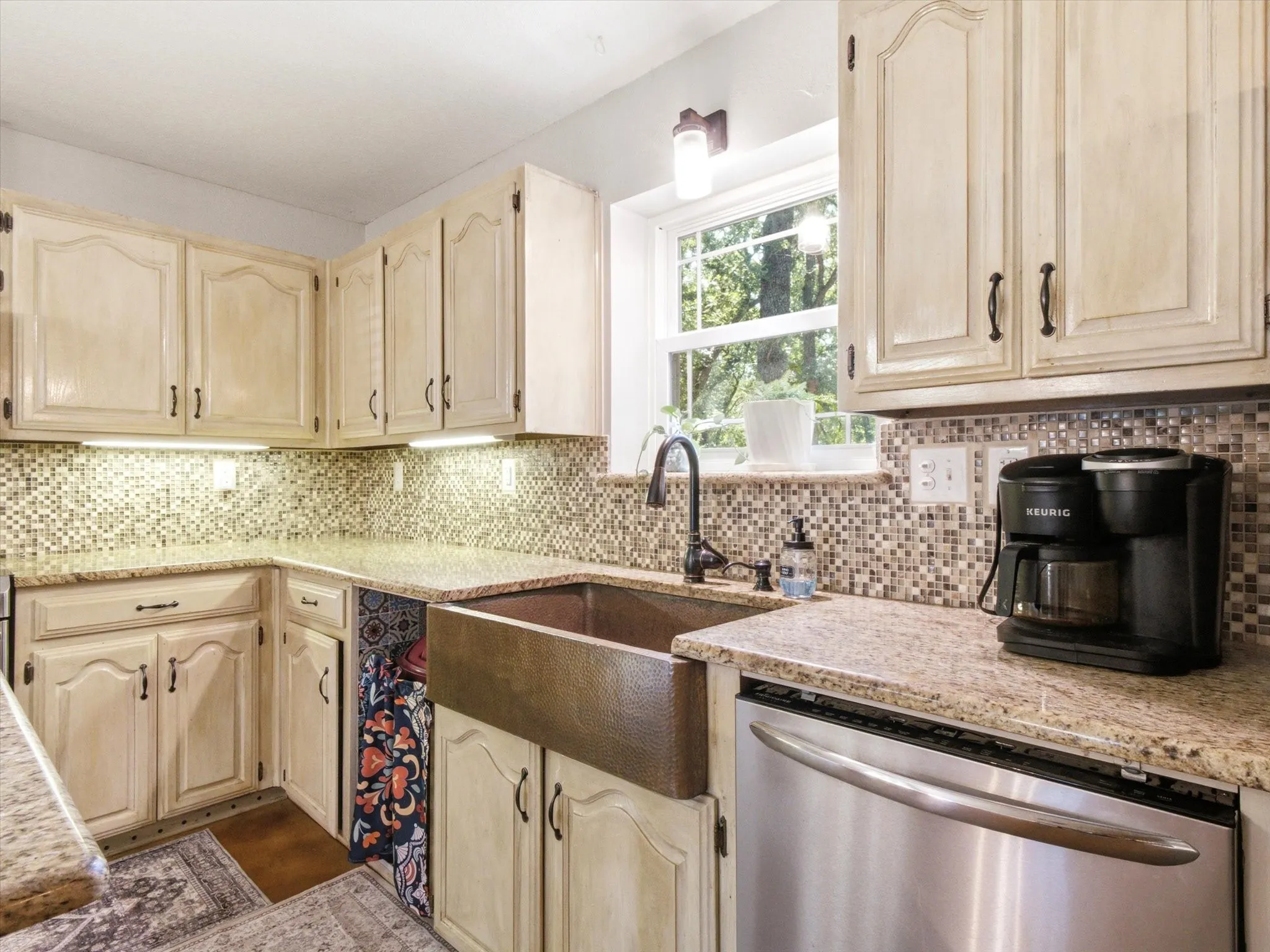 Kitchen featuring light-toned cabinetry, a mosaic tile backsplash, granite countertops, a farmhouse-style copper sink, and stainless steel dishwasher