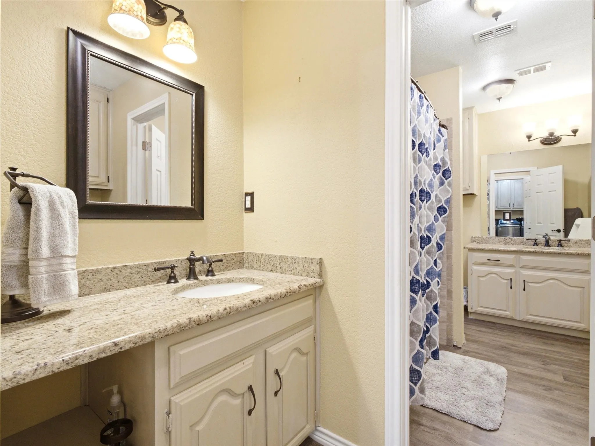 Bathroom featuring a light-toned vanity with an integrated sink, granite-style countertop, and dark-finished hardware