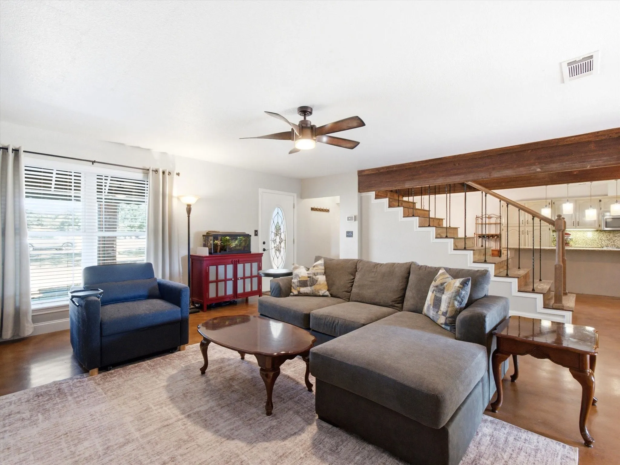Spacious living area featuring polished concrete flooring, a decorative wooden beam, and a staircase with wrought iron balusters