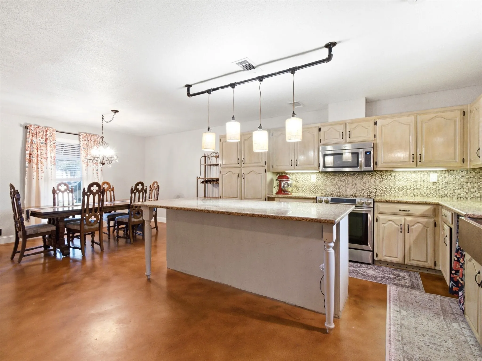 Kitchen featuring a central island with granite countertop, cream-toned cabinetry, mosaic tile backsplash, and stainless steel appliances