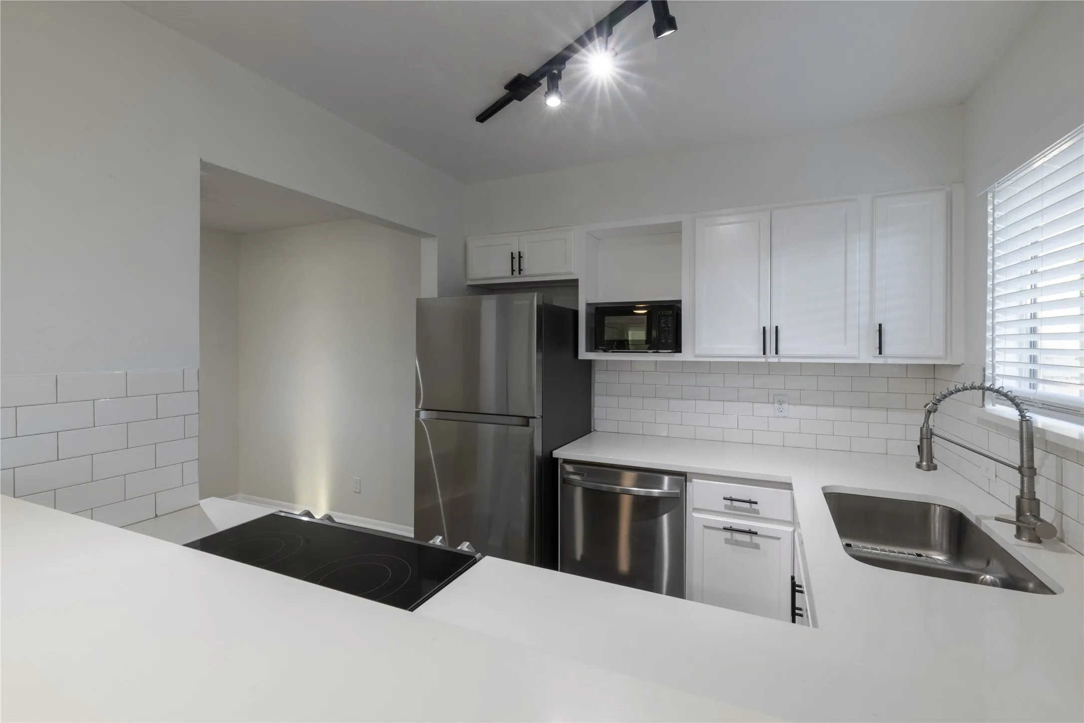 Contemporary kitchen featuring white cabinetry, stainless steel appliances, a subway tile backsplash, white countertops, and track lighting