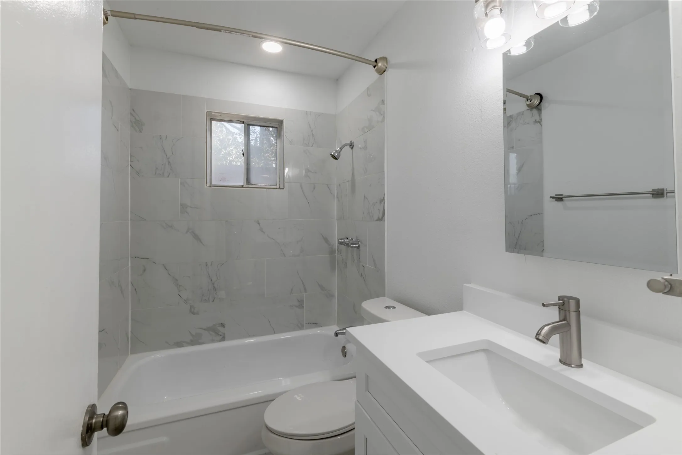 Bathroom featuring white subway tile with subtle gray veining, a white vanity with an integrated sink, a brushed nickel faucet, and a wall-mounted rectangular mirror