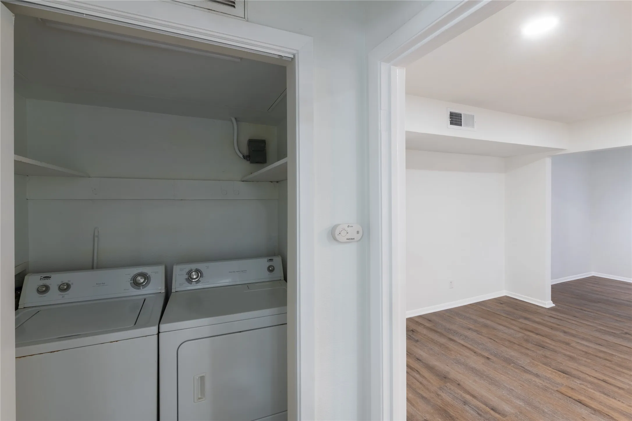 Dedicated laundry closet featuring a white washer and dryer, integrated shelving, and a bright overhead light