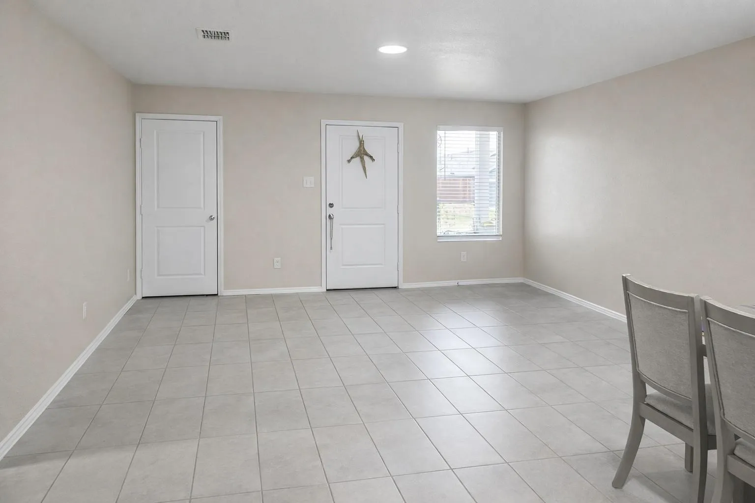Spacious living area featuring light-toned walls, tile flooring, and multiple white panel doors