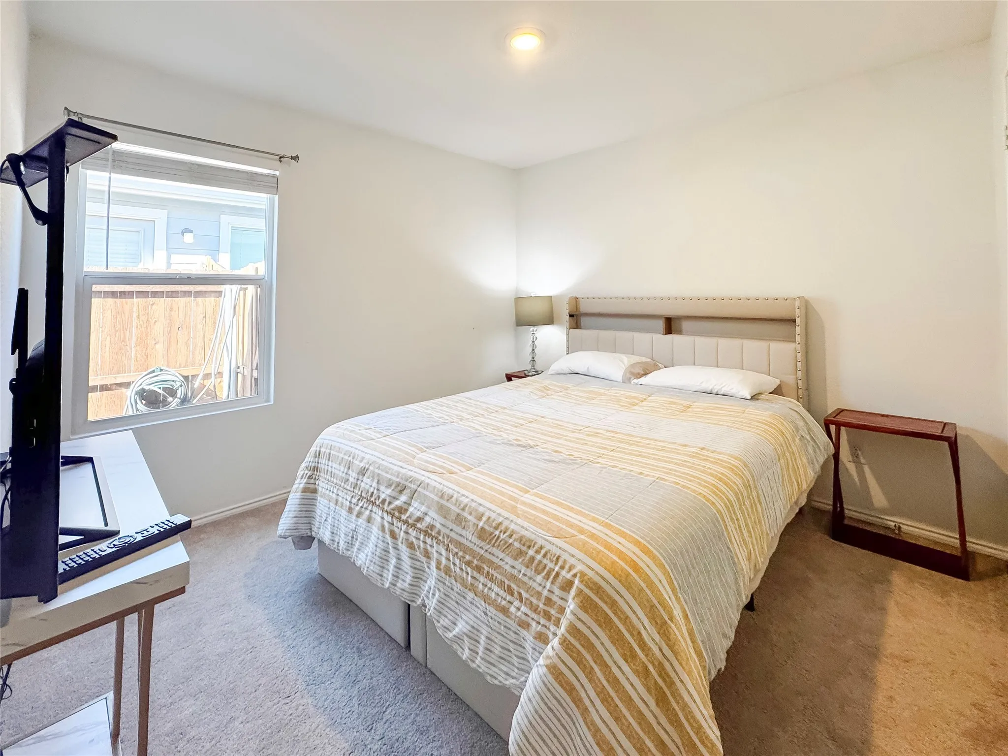Carpeted bedroom with a window featuring blinds and a privacy fence visible outside