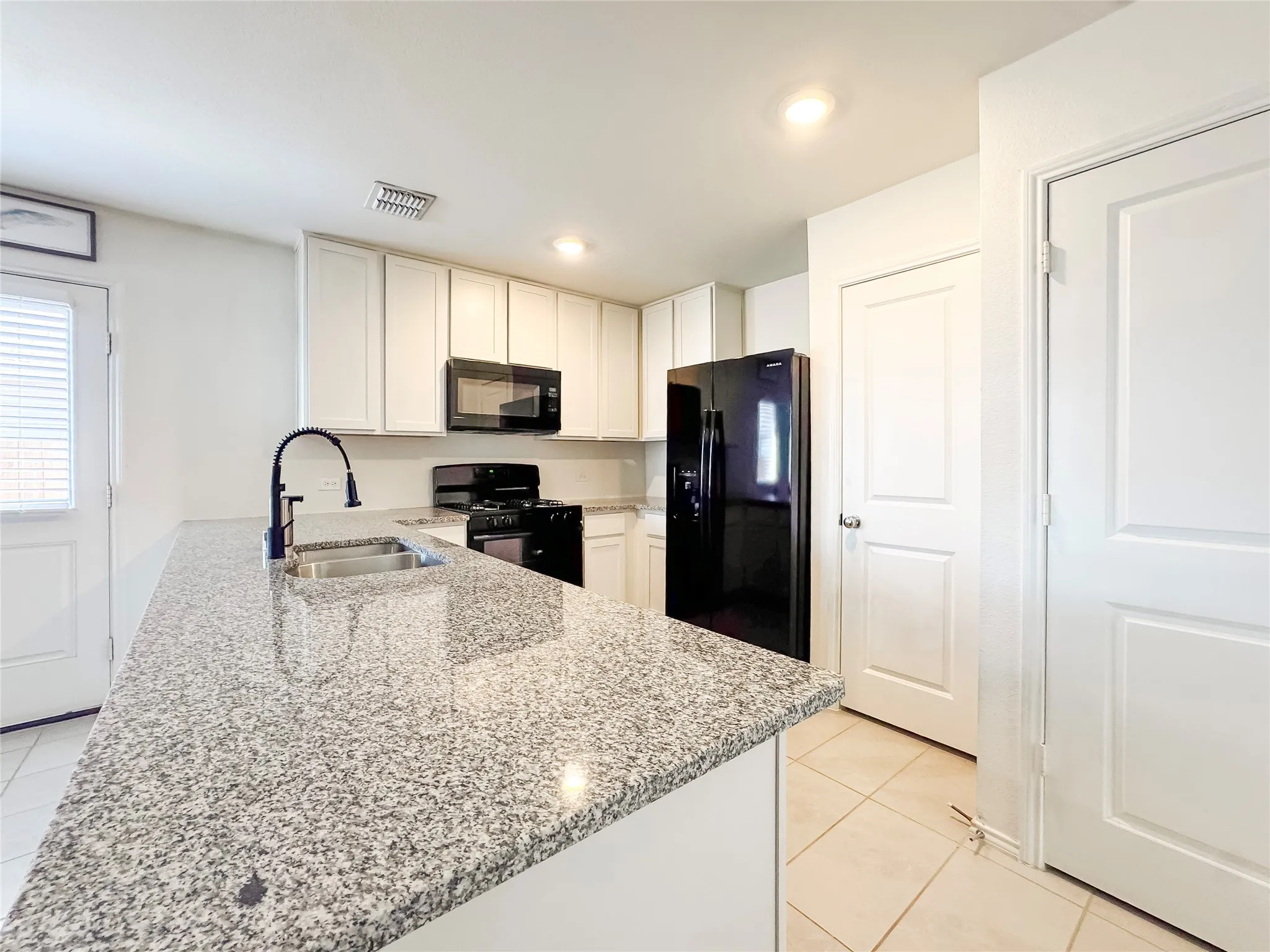 Kitchen featuring an island with a stainless steel sink, black gooseneck faucet, and granite countertop