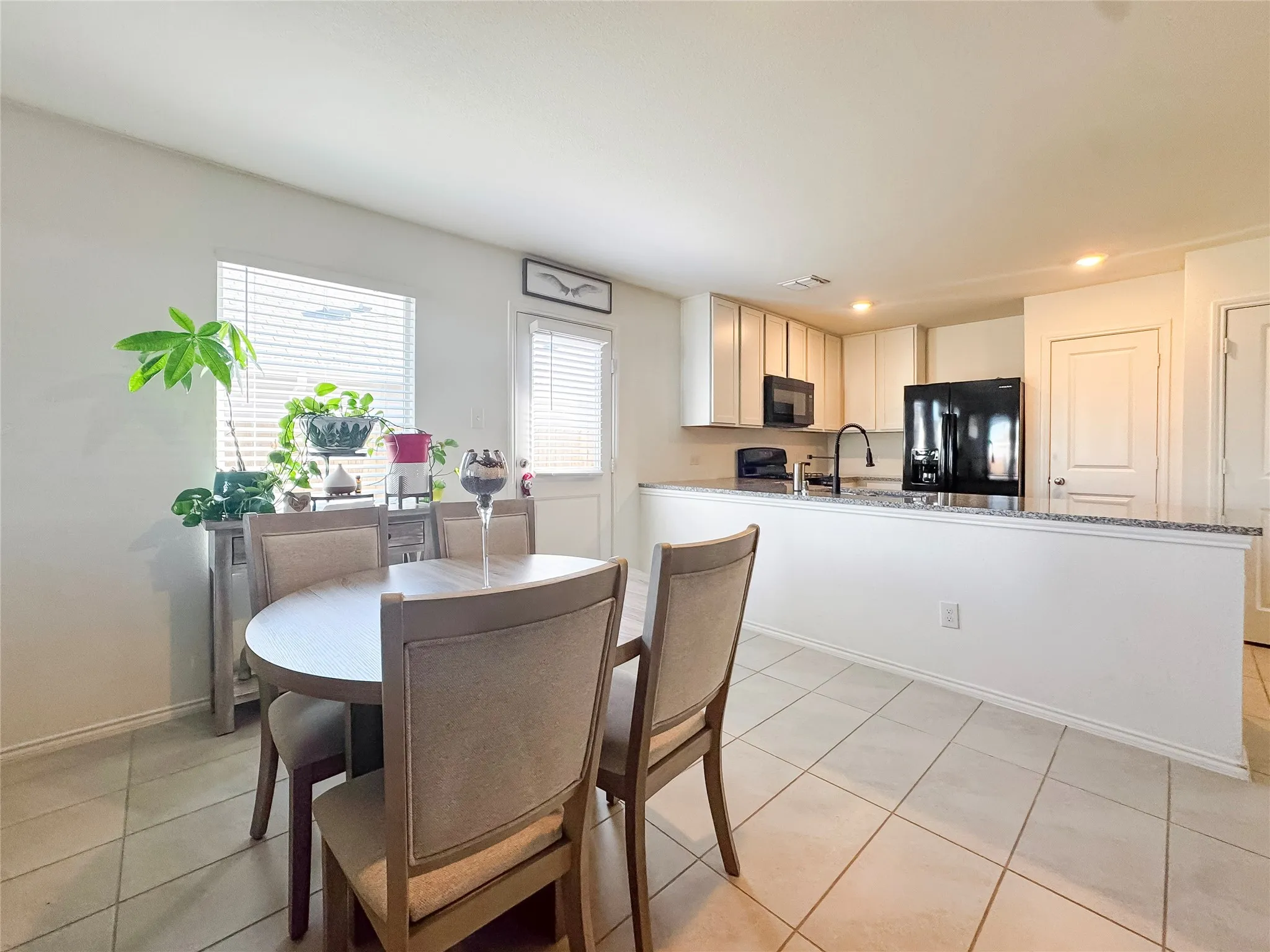 Kitchen and dining area featuring tile flooring, white cabinetry, black appliances, and granite-style countertops