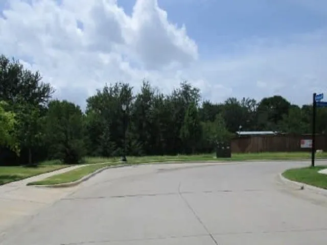 Paved street and curb featuring a grass median and mature trees
