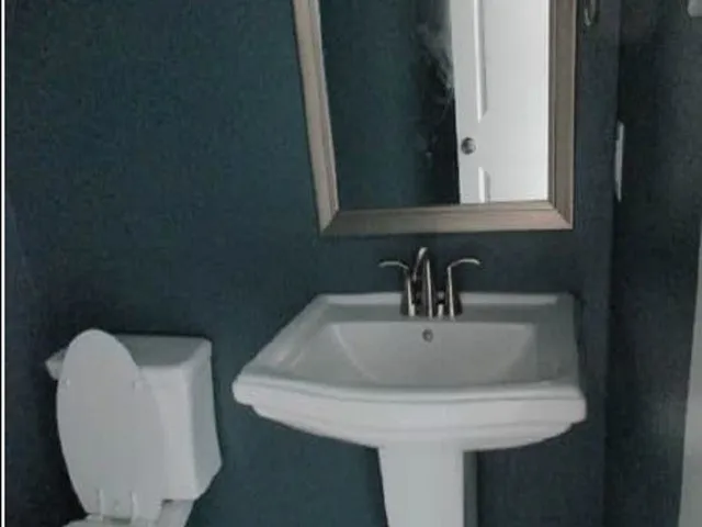 Pedestal sink with chrome-finish faucet and framed wall mirror