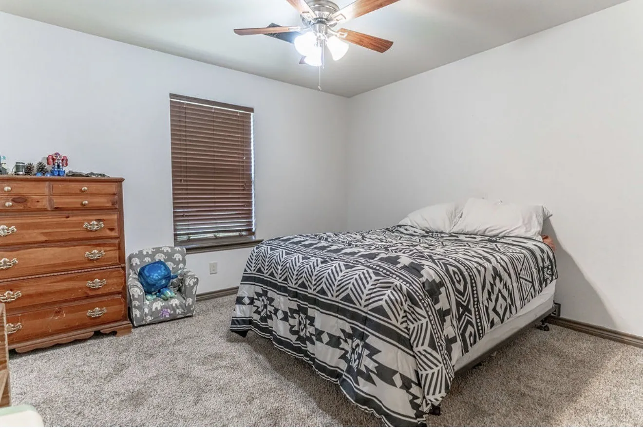 Room featuring light gray carpet flooring, white walls, and a window with wood-finish blinds