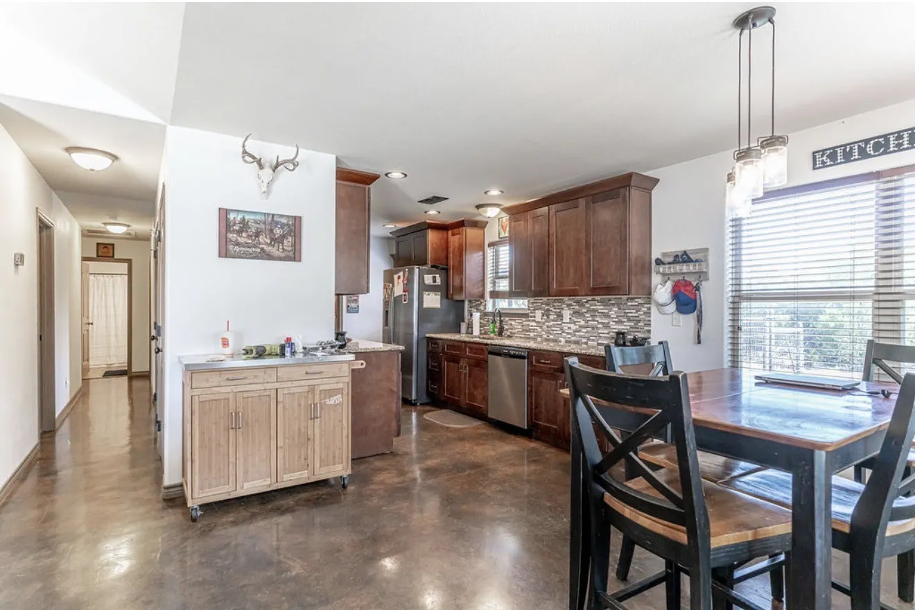 Kitchen and dining area featuring dark wood-finish cabinetry, stainless steel appliances, a tiled backsplash, and concrete flooring