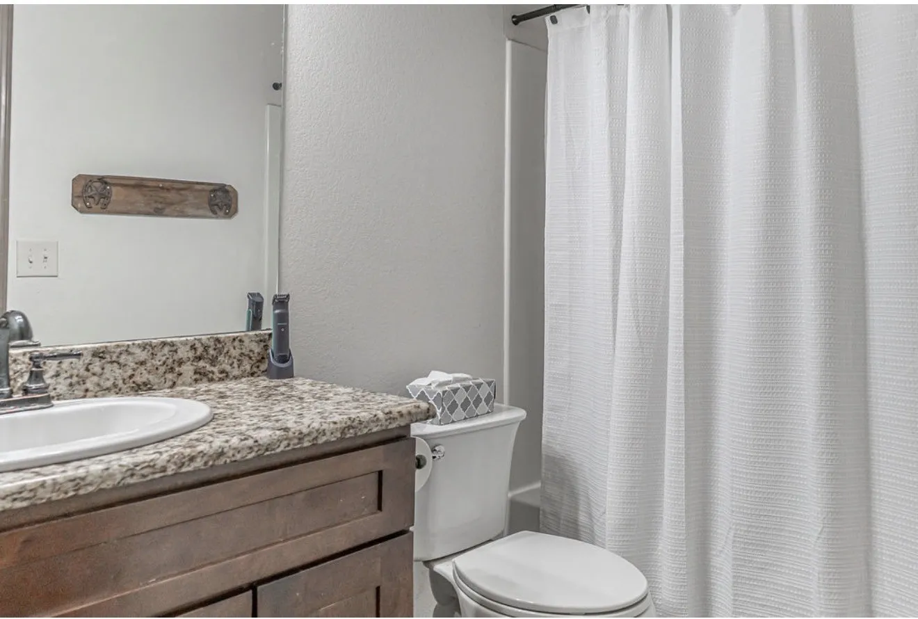 Bathroom featuring a wood-finish vanity with an undermount sink, a flecked countertop, and a shower/tub combination with a white curtain