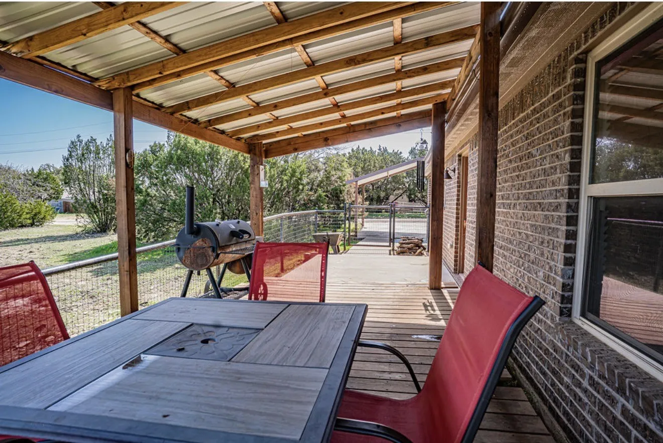 Expansive covered wooden deck featuring a metal roof, wood support beams, and a brick exterior wall