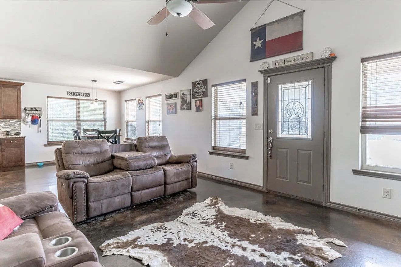 Living area featuring vaulted ceilings, dark-finish flooring, a front entry door with decorative glass, and multiple windows with blinds