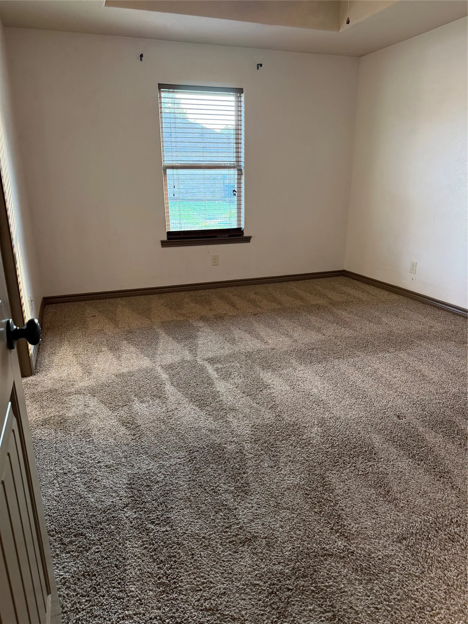 Carpeted room featuring a single window with blinds, white walls, and dark baseboards