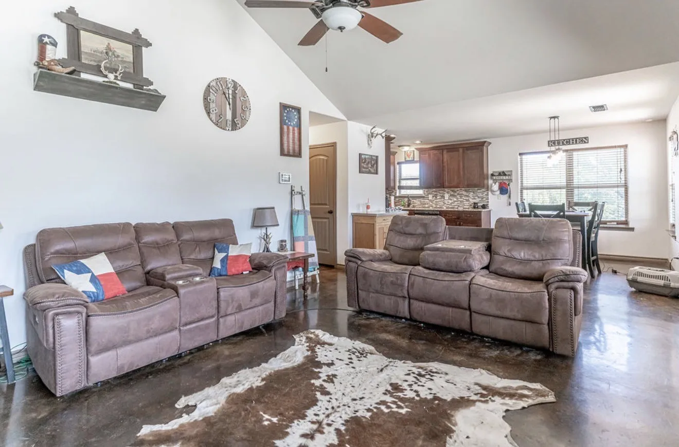 Spacious living area featuring polished concrete flooring, a vaulted ceiling with a ceiling fan, and an open-concept design to the kitchen and dining area