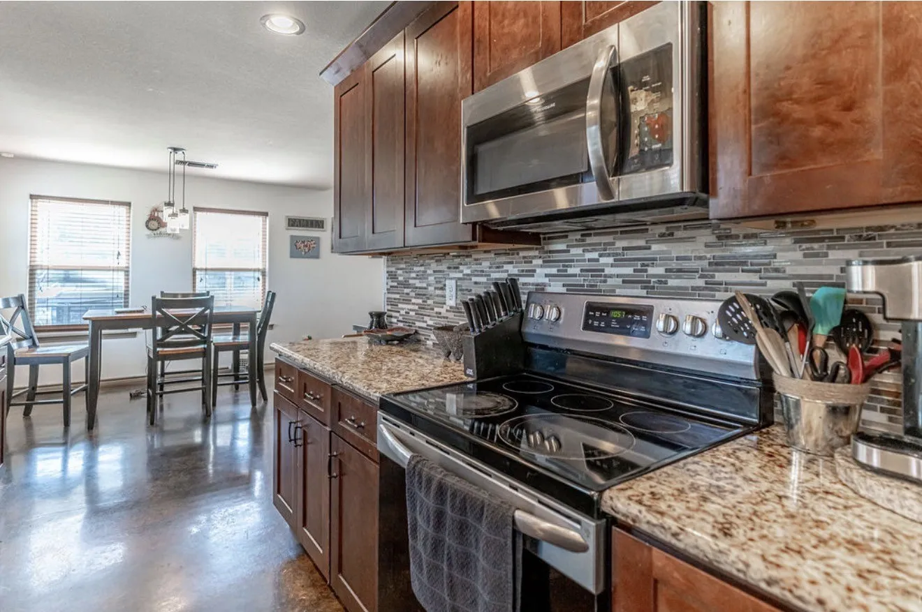 Kitchen featuring stone-finish countertops, dark wood cabinetry, a tile backsplash, and stainless steel appliances
