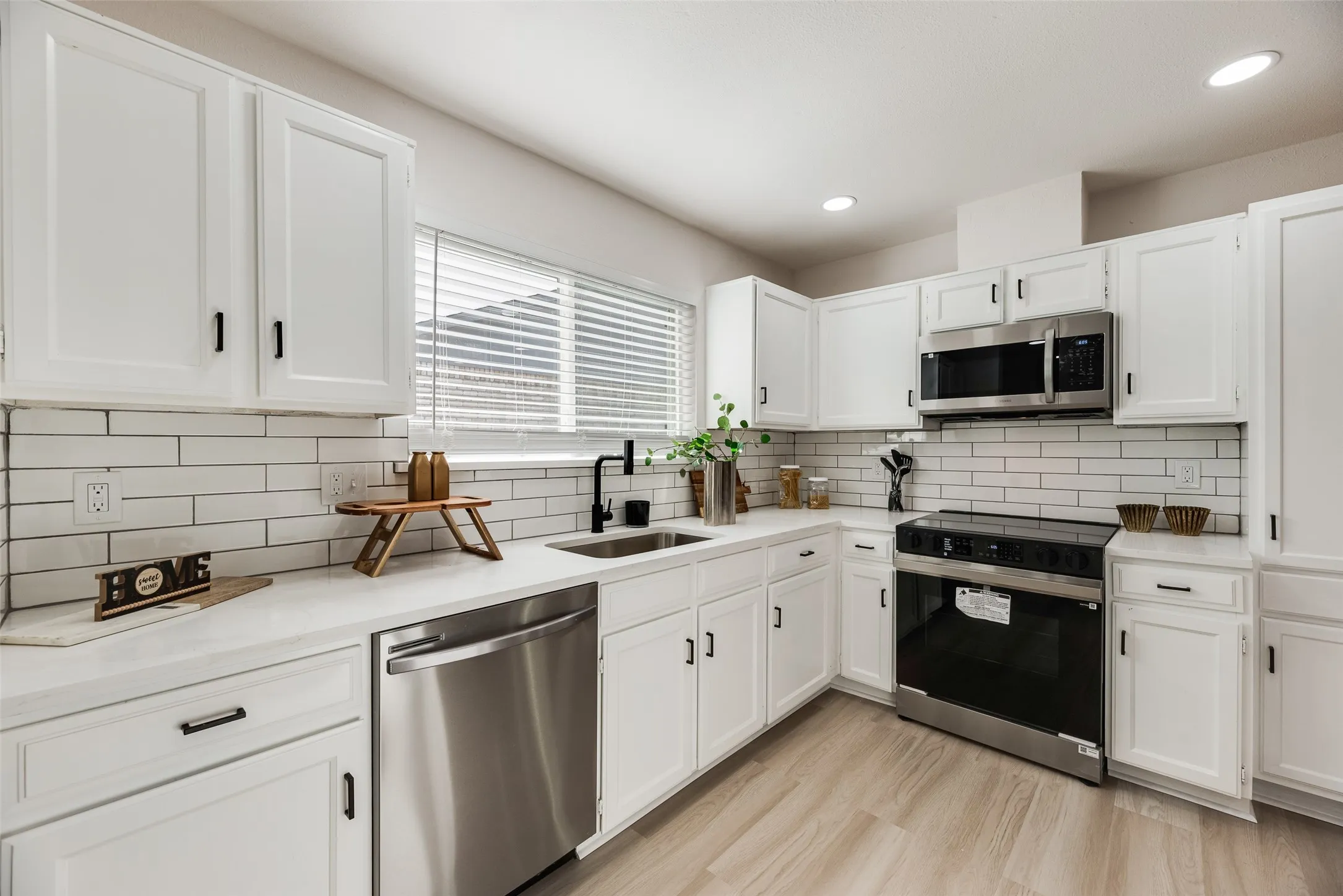 Bright, modern kitchen featuring white shaker-style cabinetry, white subway tile backsplash, and stainless steel appliances including a double wall oven, dishwasher, and microwave