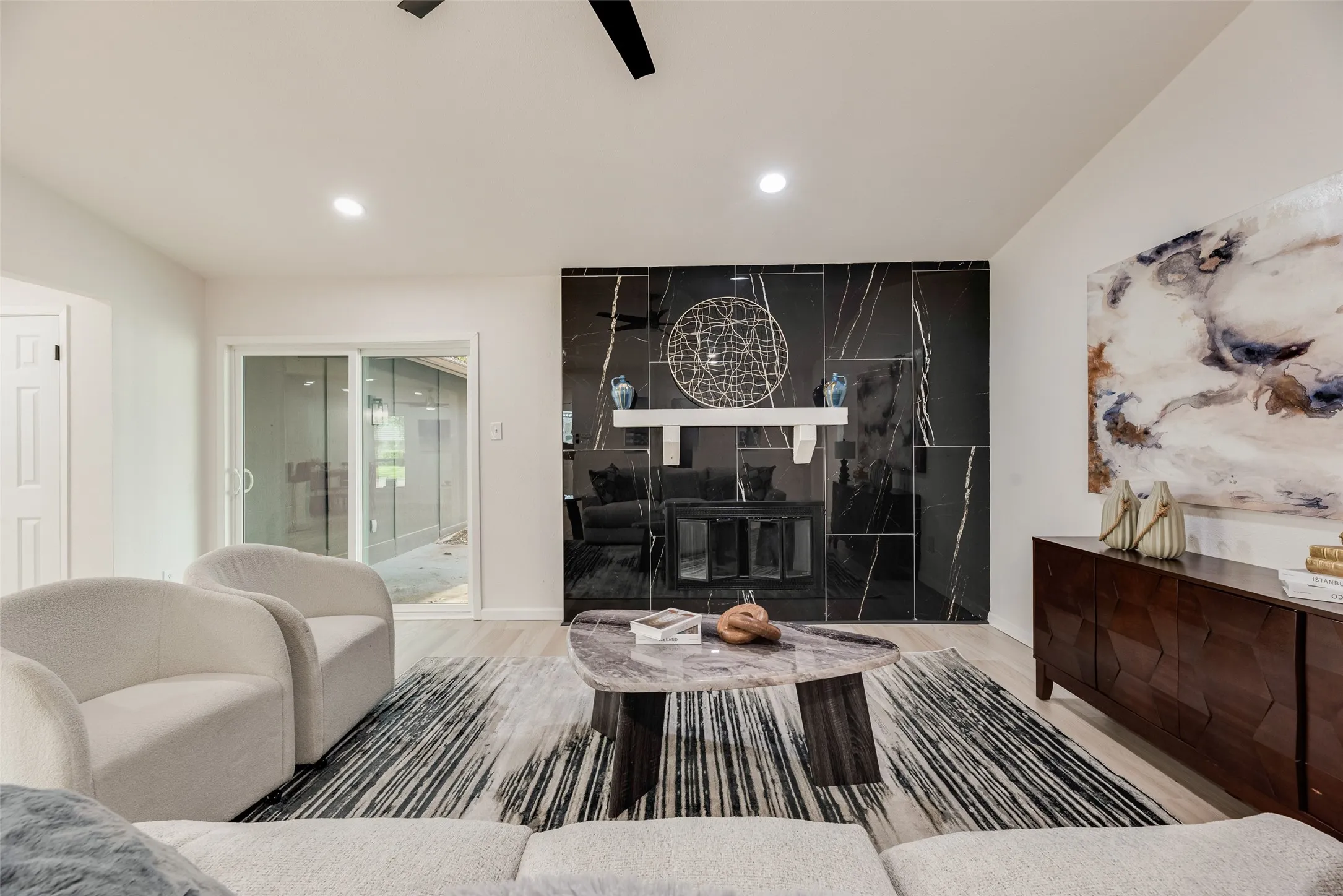 Living space featuring a striking black marble-look fireplace surround with a white mantel, ceiling-mounted lighting, and wood-finish flooring
