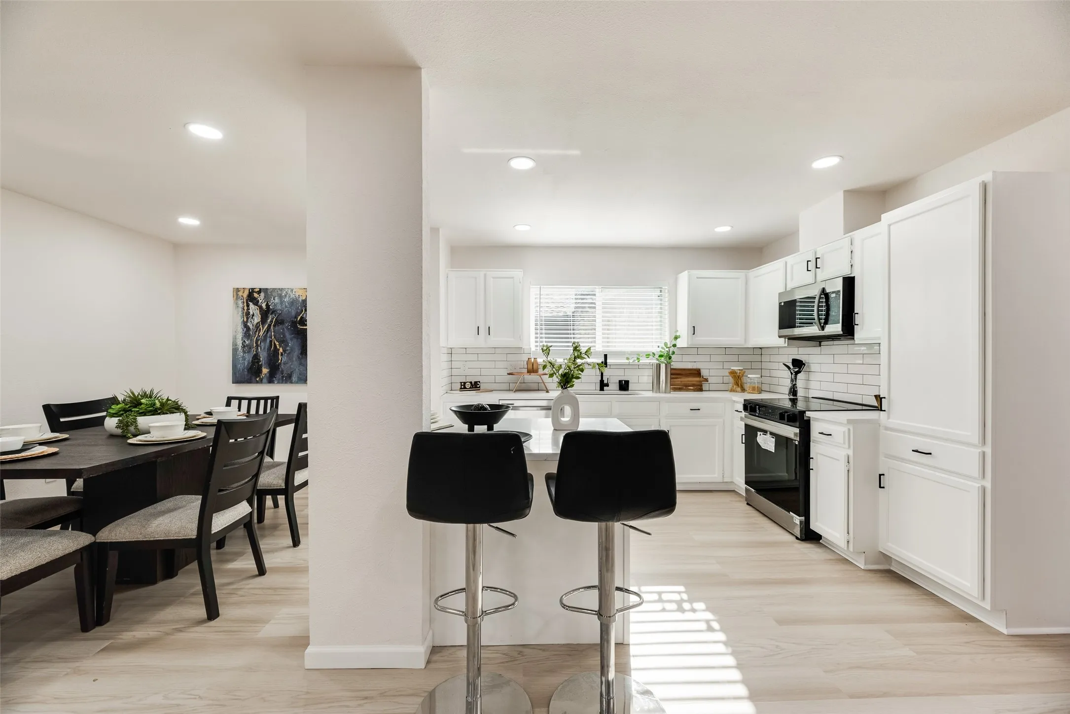 Modern kitchen featuring white cabinetry, subway tile backsplash, stainless steel appliances, and a central island with bar seating